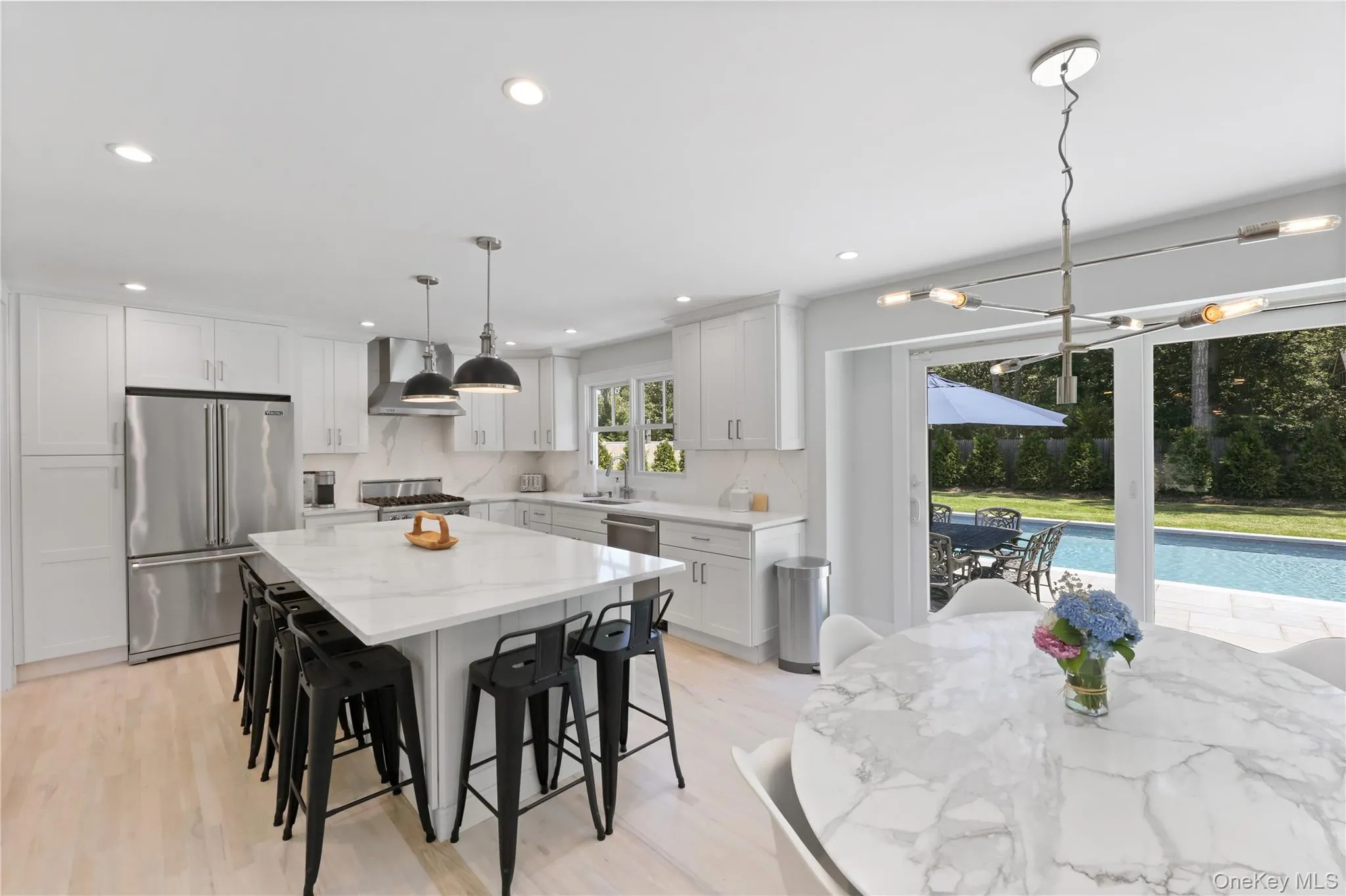 Kitchen featuring stainless steel appliances, hanging light fixtures, wall chimney exhaust hood, a kitchen breakfast bar, and light wood finished floors Kitchen featuring stainless steel appliances, hanging light fixtures, wall chimney exhaust hood, a kitchen breakfast bar, and light wood finished floors