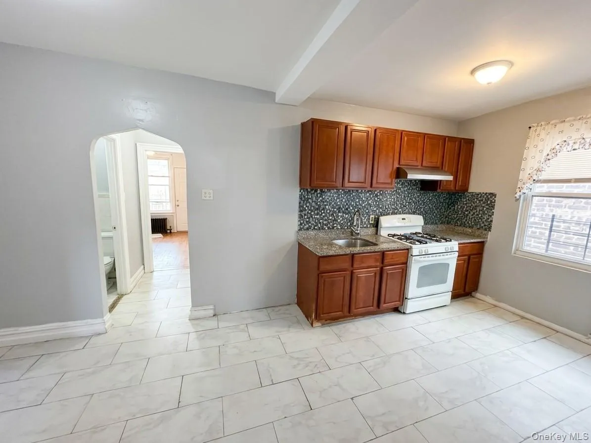 Kitchen featuring wood cabinetry, a gas range, stainless steel sink, and mosaic tile backsplash Kitchen featuring wood cabinetry, a gas range, stainless steel sink, and mosaic tile backsplash