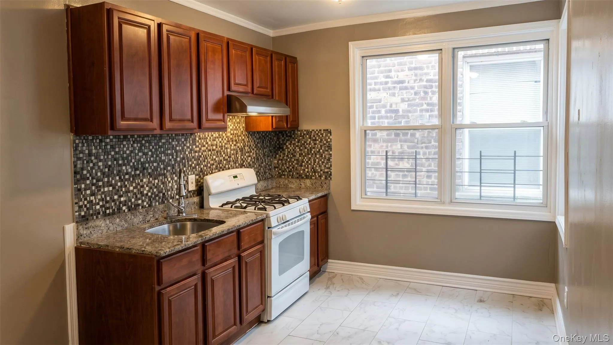 Kitchen featuring wood-finish cabinetry, mosaic tile backsplash, granite-style countertops, and a double-pane window Kitchen featuring wood-finish cabinetry, mosaic tile backsplash, granite-style countertops, and a double-pane window