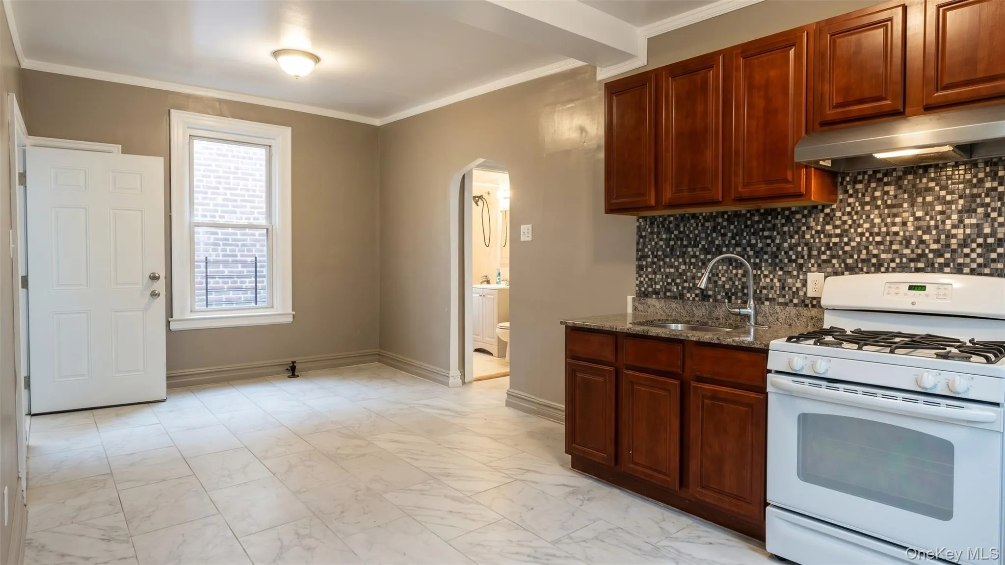 Kitchen featuring wood-finish cabinetry, mosaic tile backsplash, granite-style countertops, and a double-pane window Kitchen featuring wood-finish cabinetry, mosaic tile backsplash, granite-style countertops, and a double-pane window