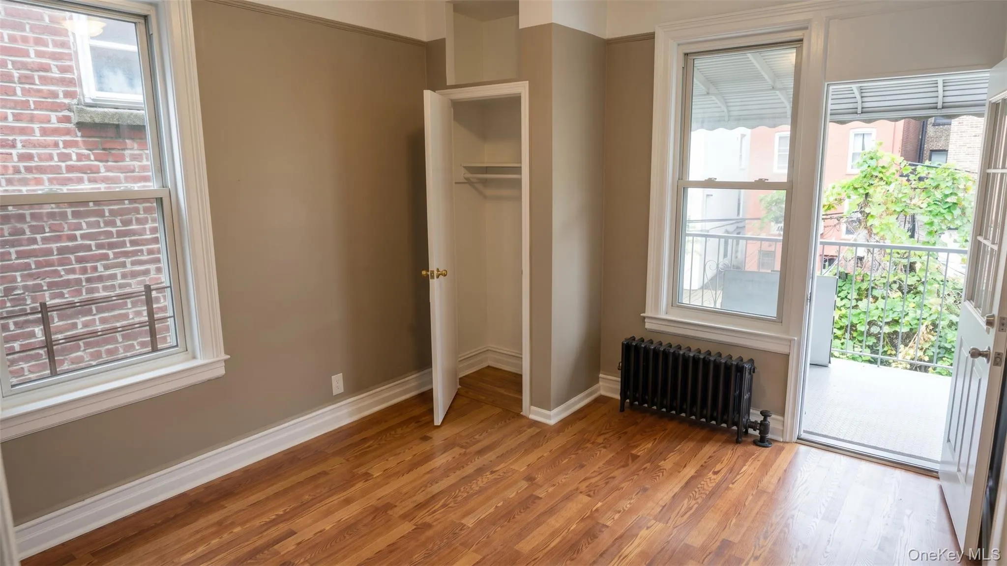 Hardwood-style flooring, white trim, built-in closet with hanging rod, window with natural light, a white paneled door and a private balcony with a metal railing Hardwood-style flooring, white trim, built-in closet with hanging rod, window with natural light, a white paneled door and a private balcony with a metal railing