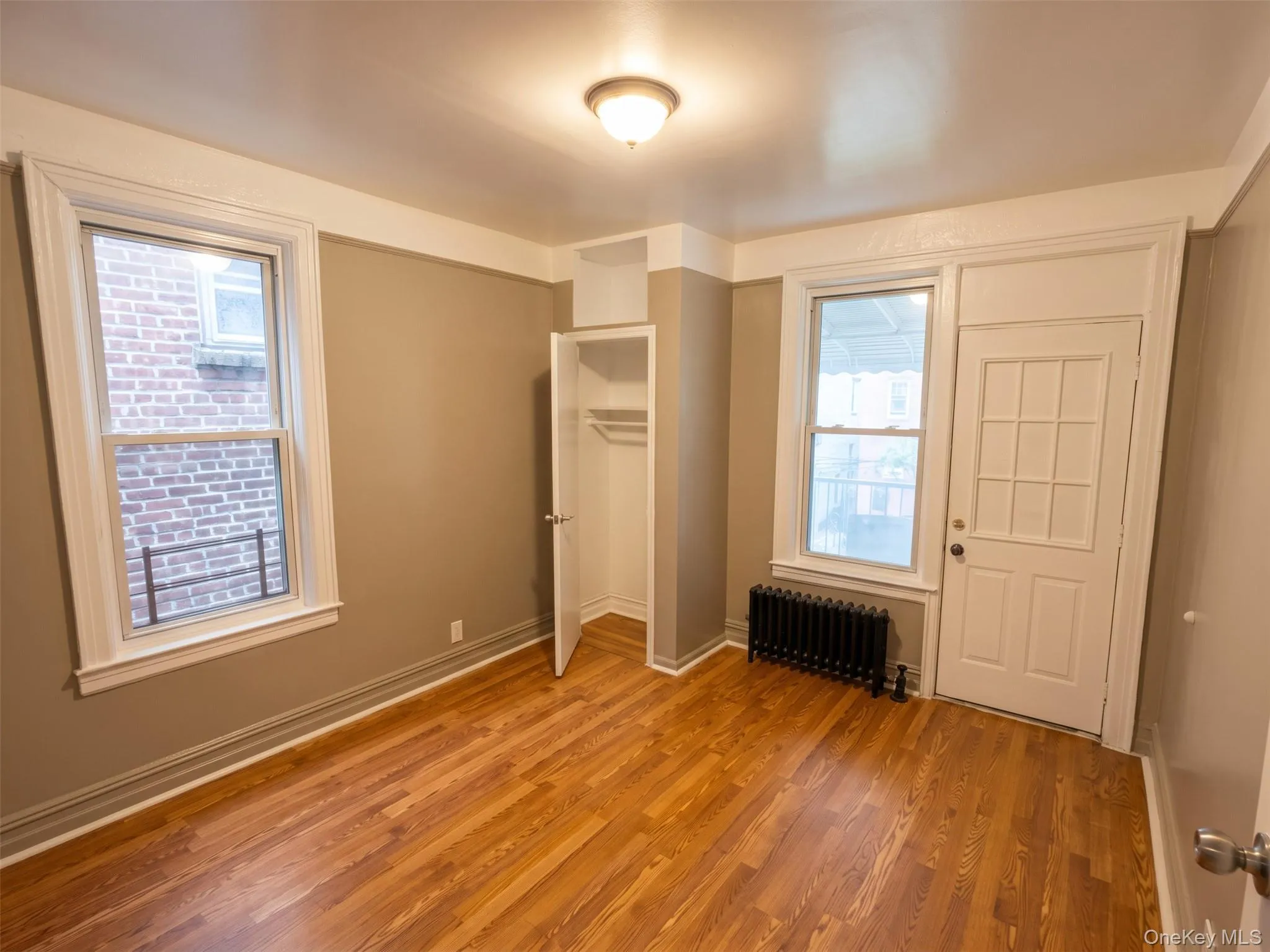 Hardwood-style flooring, white trim, built-in closet with hanging rod, window with natural light, a white paneled door and a private balcony with a metal railing Hardwood-style flooring, white trim, built-in closet with hanging rod, window with natural light, a white paneled door and a private balcony with a metal railing