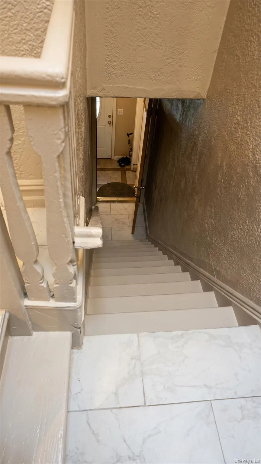 Staircase with painted wood handrail, textured walls, and tile flooring Staircase with painted wood handrail, textured walls, and tile flooring