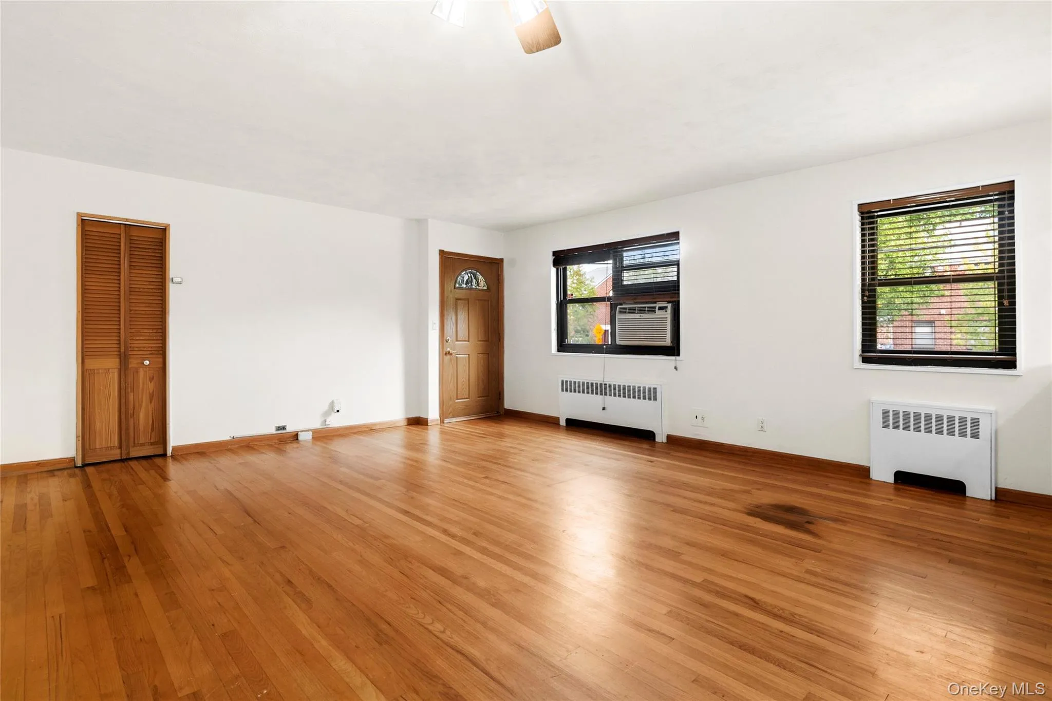 Hardwood flooring, wood-paneled entry door, two windows with blinds, and white wall finishes Hardwood flooring, wood-paneled entry door, two windows with blinds, and white wall finishes
