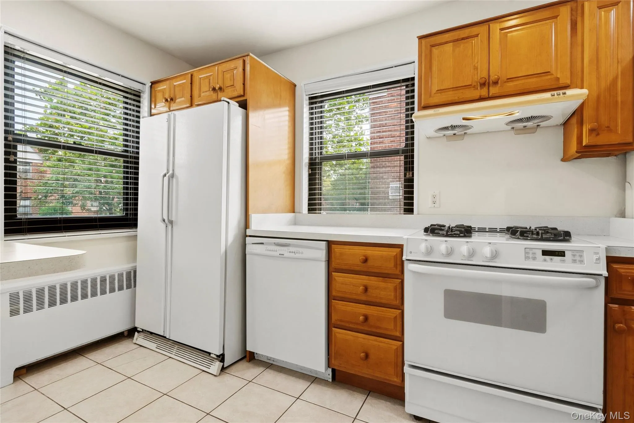 Kitchen featuring wood cabinetry, white appliances, white countertops, and tiled flooring Kitchen featuring wood cabinetry, white appliances, white countertops, and tiled flooring