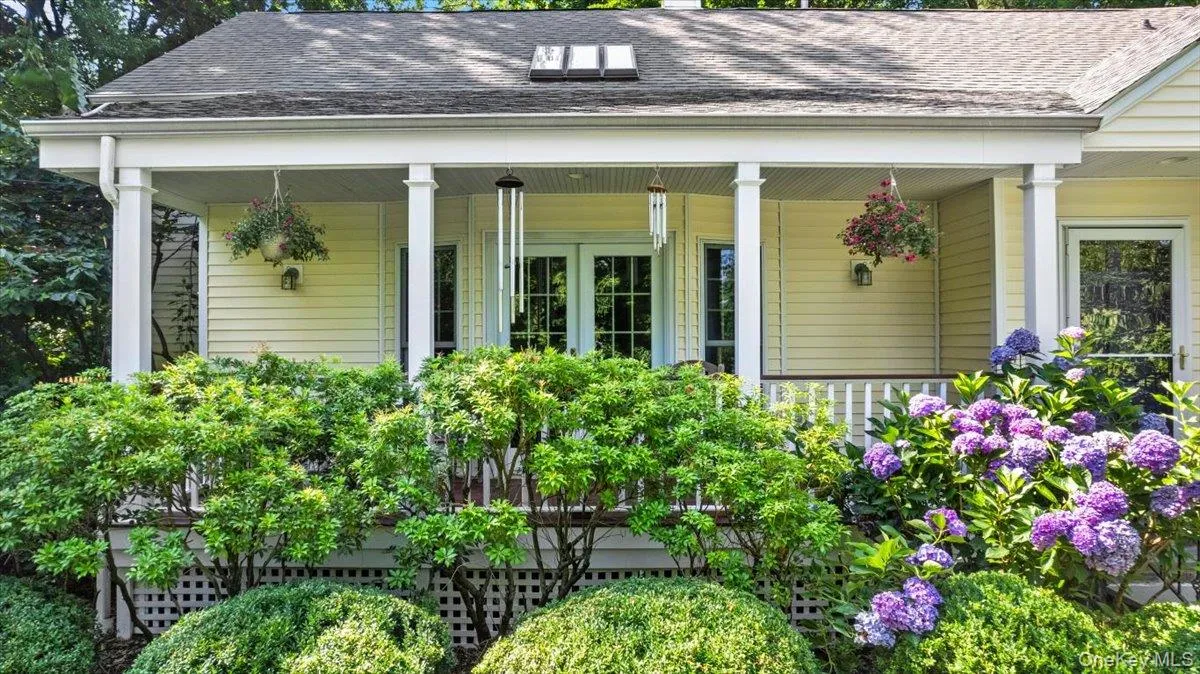 View of charming front porch with white columns, double glass panel doors, and mature landscaping View of charming front porch with white columns, double glass panel doors, and mature landscaping