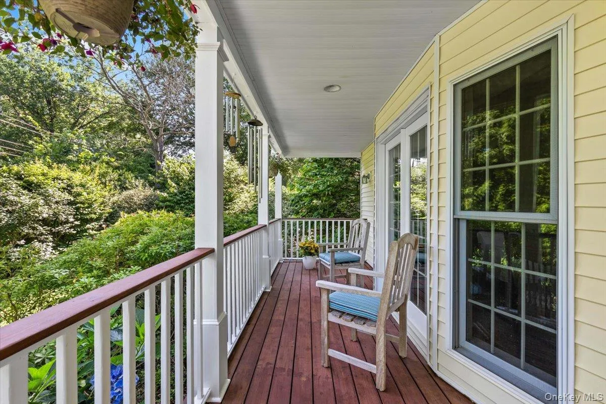 Expansive covered porch featuring wood-finish decking, white railings with a dark wood-finish top rail, and light yellow siding Expansive covered porch featuring wood-finish decking, white railings with a dark wood-finish top rail, and light yellow siding