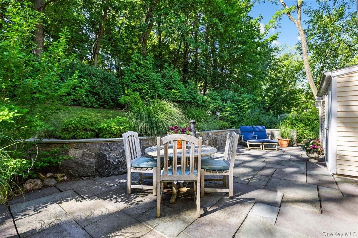 Expansive stone patio featuring a dining area, natural stone retaining wall, and lush landscaping Expansive stone patio featuring a dining area, natural stone retaining wall, and lush landscaping