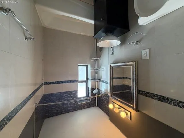 Bathroom featuring a white bathtub, white wall tiles with decorative blue accents, a pedestal sink with a dark cabinet, and a window for natural light Bathroom featuring a white bathtub, white wall tiles with decorative blue accents, a pedestal sink with a dark cabinet, and a window for natural light