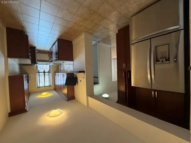 Modern kitchen featuring wood-finish cabinetry, stainless steel refrigerator, granite countertops, and tiled flooring Modern kitchen featuring wood-finish cabinetry, stainless steel refrigerator, granite countertops, and tiled flooring
