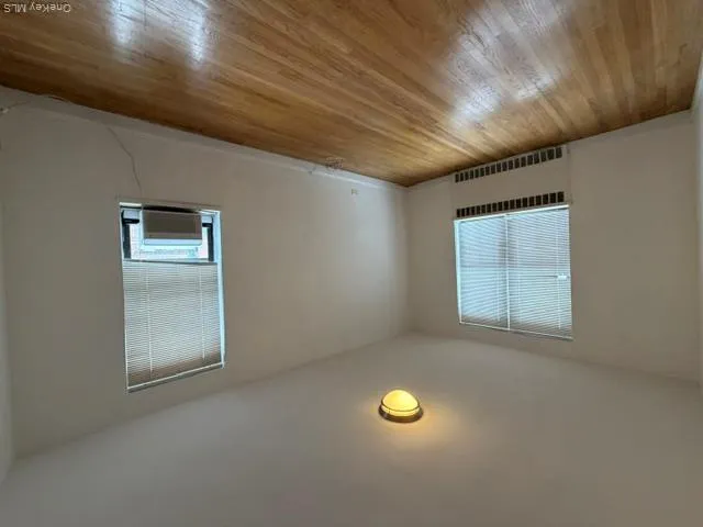 Hardwood flooring, two windows with blinds, wall-mounted heating unit, and an installed window air conditioning unit Hardwood flooring, two windows with blinds, wall-mounted heating unit, and an installed window air conditioning unit