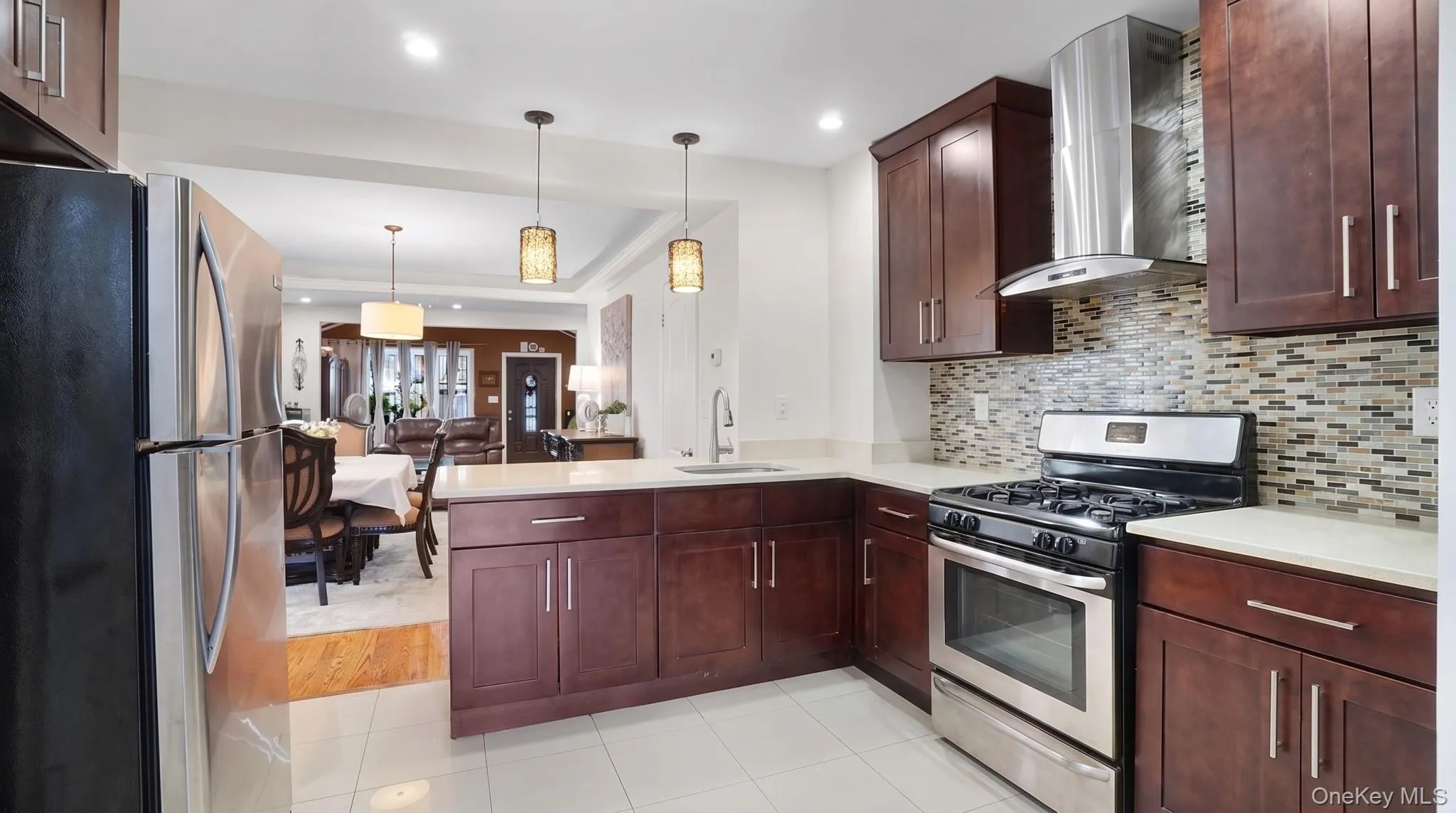 Kitchen featuring dark wood cabinetry, light-toned countertops, stainless steel appliances, a mosaic tile backsplash, and recessed lighting Kitchen featuring dark wood cabinetry, light-toned countertops, stainless steel appliances, a mosaic tile backsplash, and recessed lighting