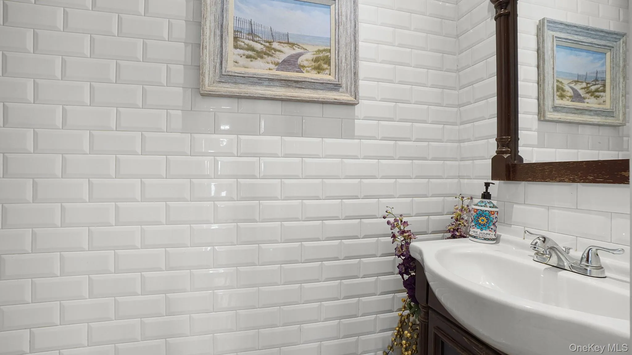 White subway tile walls with a decorative wood-framed mirror and a white ceramic sink with a chrome faucet White subway tile walls with a decorative wood-framed mirror and a white ceramic sink with a chrome faucet
