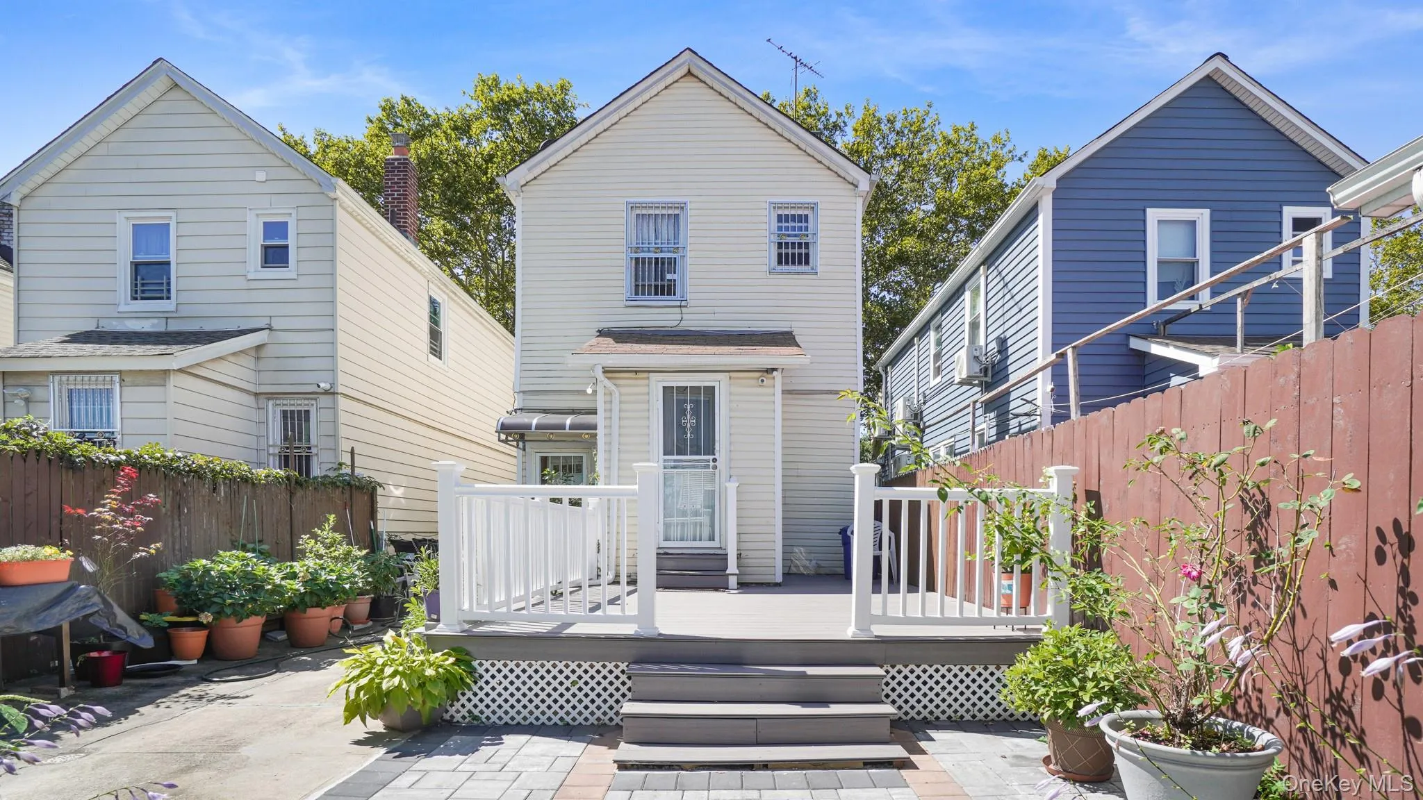 Rear deck with white railings and lattice skirting, featuring steps to a paved patio Rear deck with white railings and lattice skirting, featuring steps to a paved patio