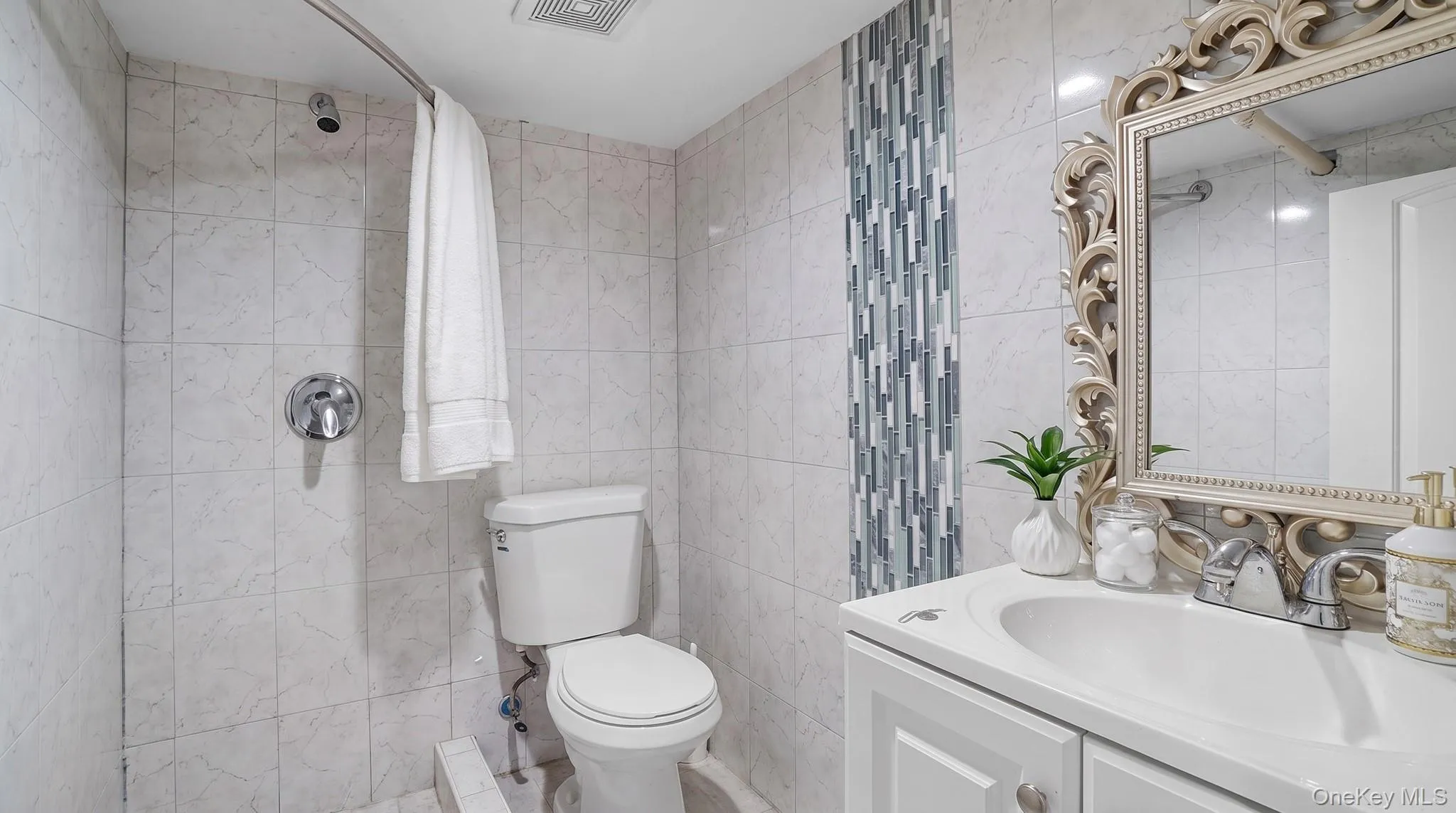 Tiled shower with chrome fixtures, vanity with integrated sink, and an ornate framed mirror Tiled shower with chrome fixtures, vanity with integrated sink, and an ornate framed mirror
