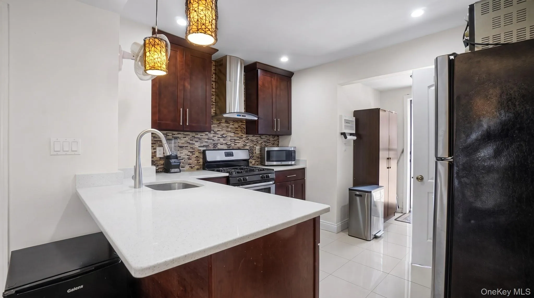 Kitchen featuring dark wood cabinetry, a mosaic tile backsplash, stainless steel appliances, and light-colored countertops Kitchen featuring dark wood cabinetry, a mosaic tile backsplash, stainless steel appliances, and light-colored countertops