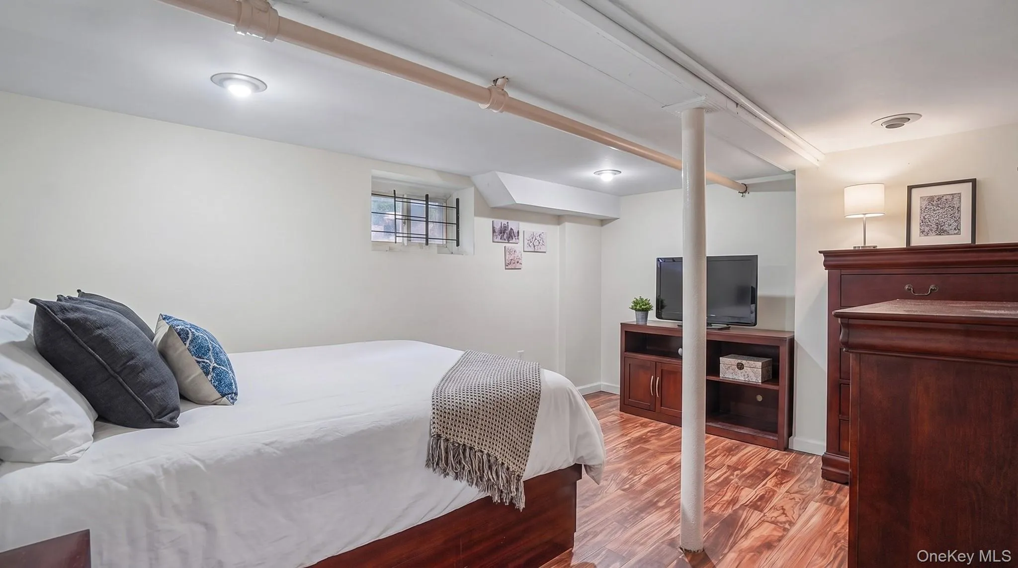 Recessed lighting, wood-finish flooring, white painted walls, and an egress window with security bars Recessed lighting, wood-finish flooring, white painted walls, and an egress window with security bars
