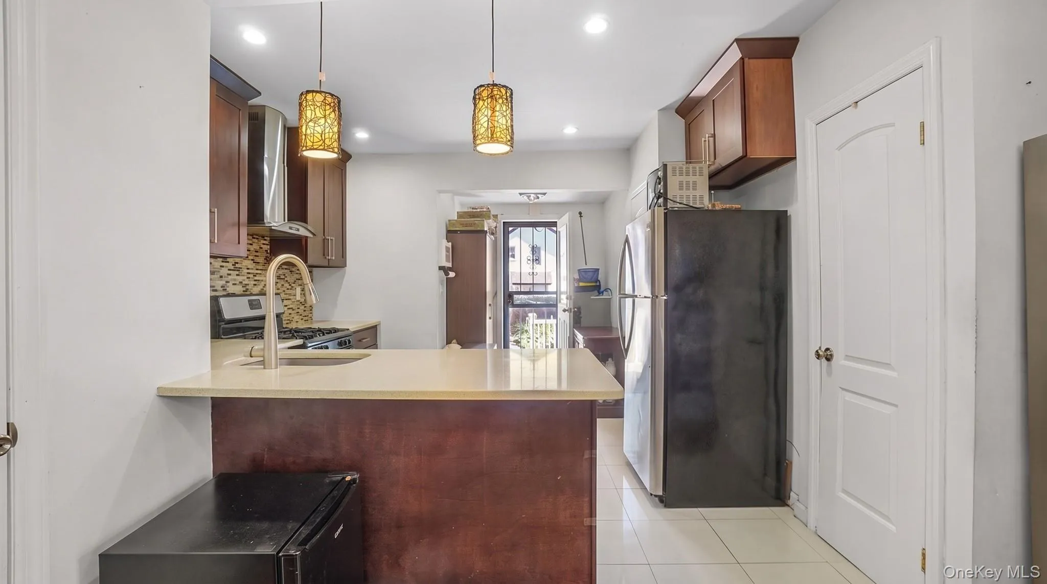 Kitchen featuring wood cabinetry, stainless steel range hood, stone-finish countertops, and decorative pendant lighting Kitchen featuring wood cabinetry, stainless steel range hood, stone-finish countertops, and decorative pendant lighting