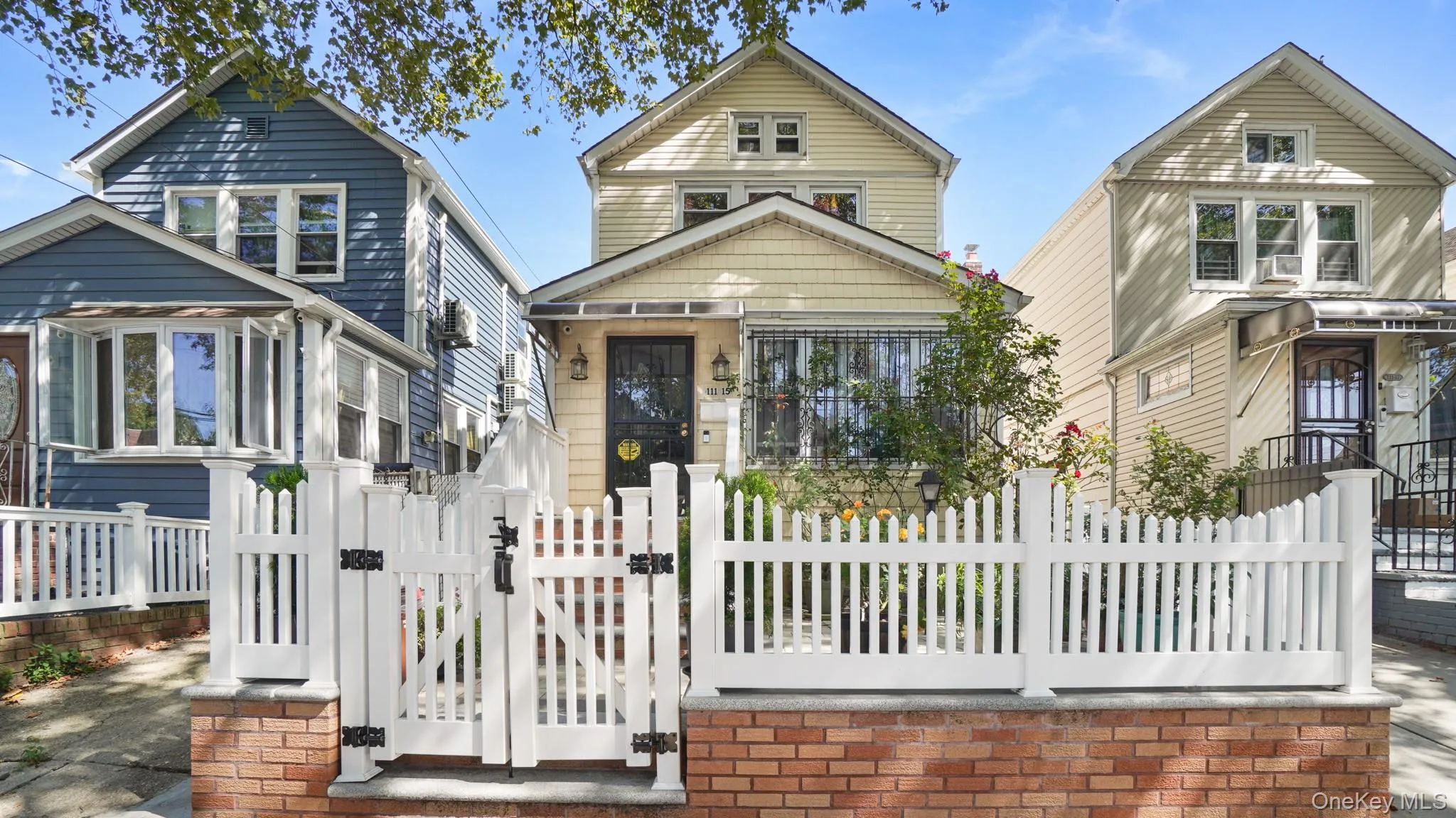 White picket fence with brick base, gabled roofline, and front garden White picket fence with brick base, gabled roofline, and front garden