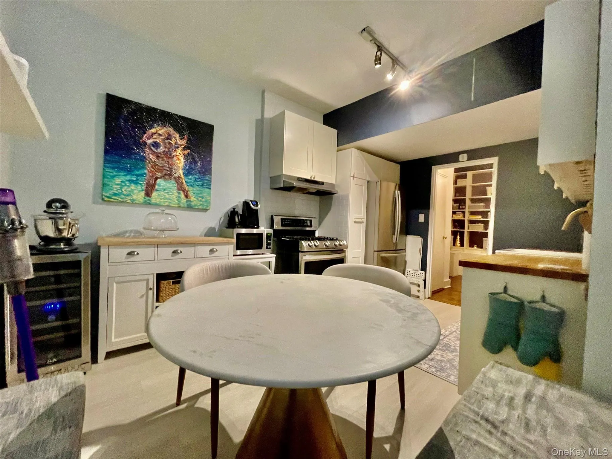 Kitchen featuring white cabinetry, stainless steel appliances, wood-finish flooring, and track lighting Kitchen featuring white cabinetry, stainless steel appliances, wood-finish flooring, and track lighting