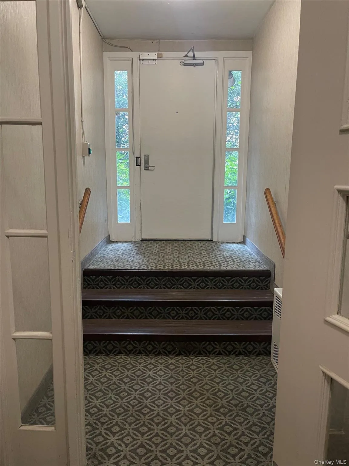 side door Entryway featuring a white door with sidelight windows, patterned floor covering, and a wooden handrail side door Entryway featuring a white door with sidelight windows, patterned floor covering, and a wooden handrail