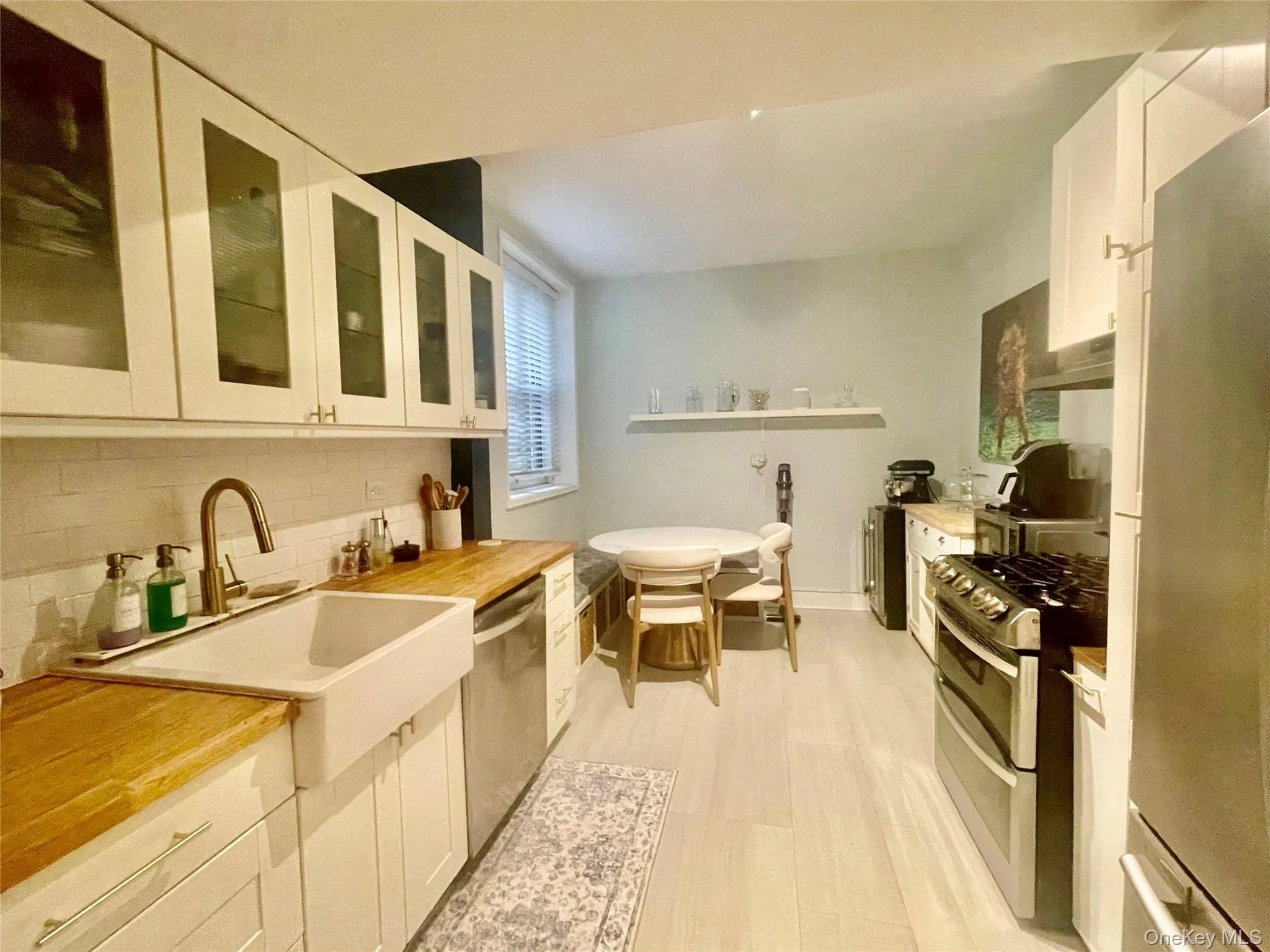 White shaker cabinetry with glass-front uppers, wood-finish countertops, and a farmhouse-style sink with a bronze-finish faucet White shaker cabinetry with glass-front uppers, wood-finish countertops, and a farmhouse-style sink with a bronze-finish faucet