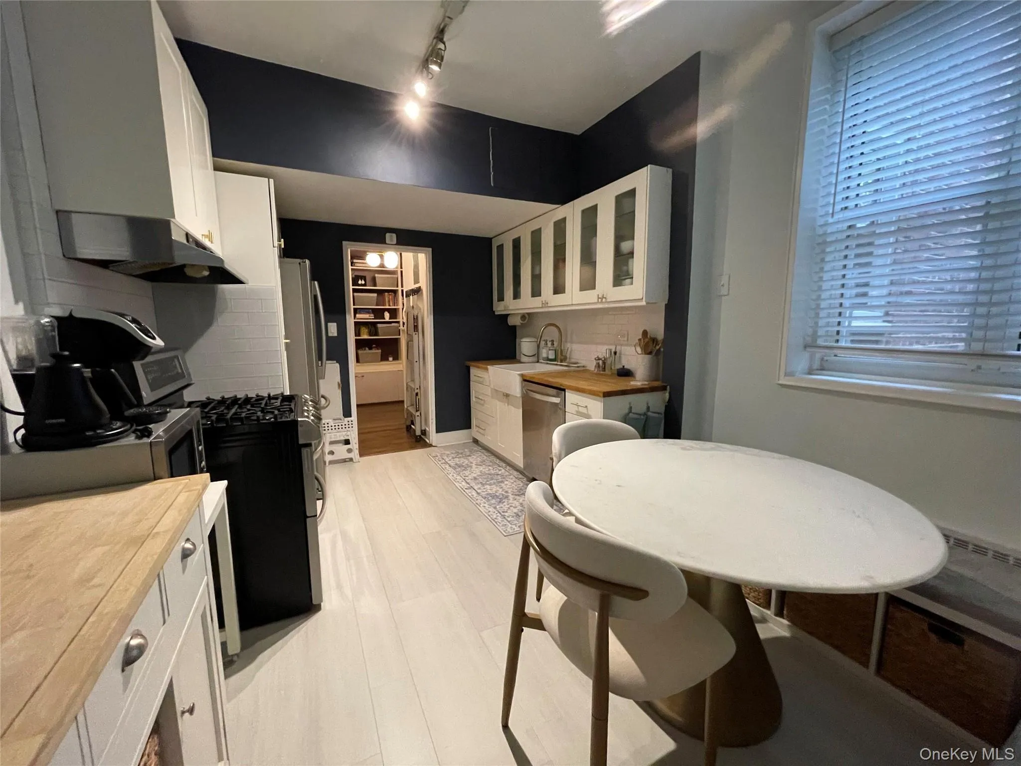 Kitchen featuring light wood-finish flooring, white cabinetry, a built-in stainless steel dishwasher, a built-in gas range, and a white subway tile backsplash Kitchen featuring light wood-finish flooring, white cabinetry, a built-in stainless steel dishwasher, a built-in gas range, and a white subway tile backsplash