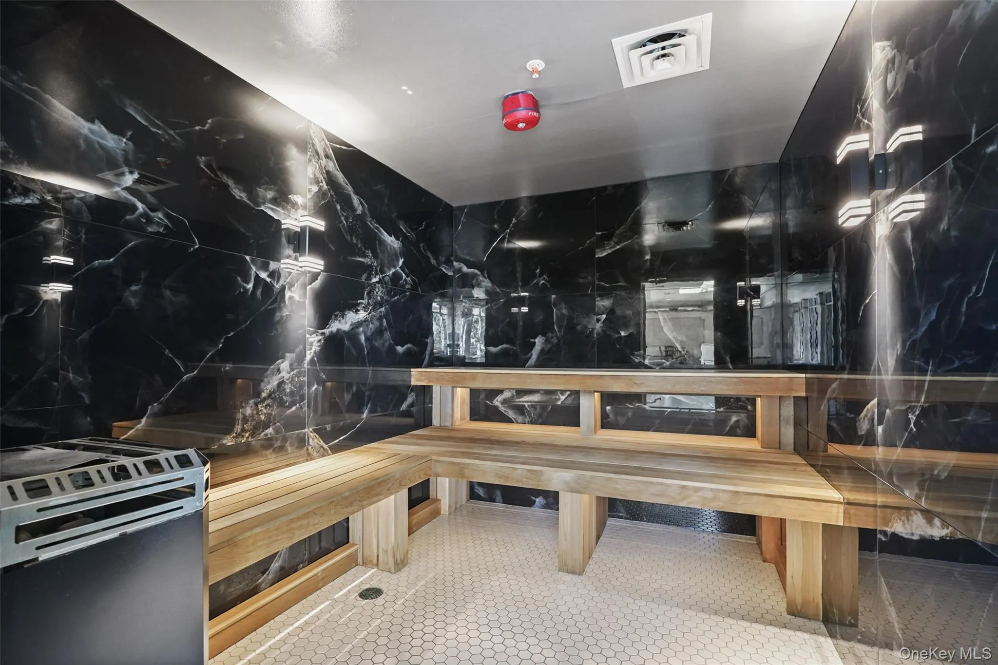 Black marble-style wall finishes, light wood benches, white hexagonal floor tiling, and a built-in heating unit Black marble-style wall finishes, light wood benches, white hexagonal floor tiling, and a built-in heating unit