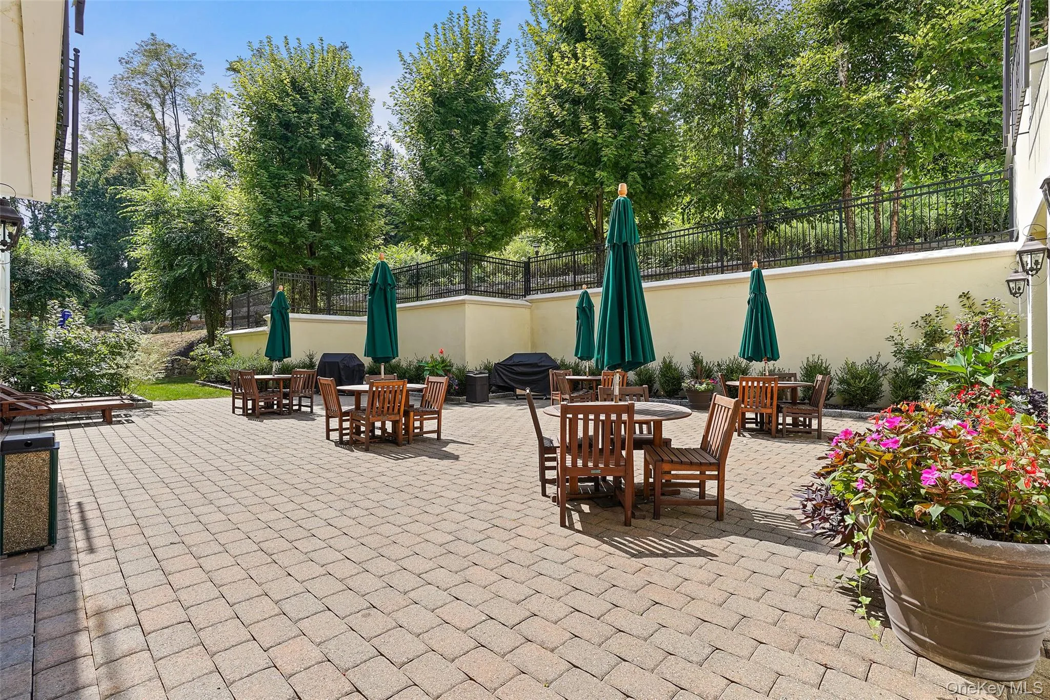 Expansive paver patio with a low retaining wall, black wrought iron fencing, mature trees, and landscaping Expansive paver patio with a low retaining wall, black wrought iron fencing, mature trees, and landscaping