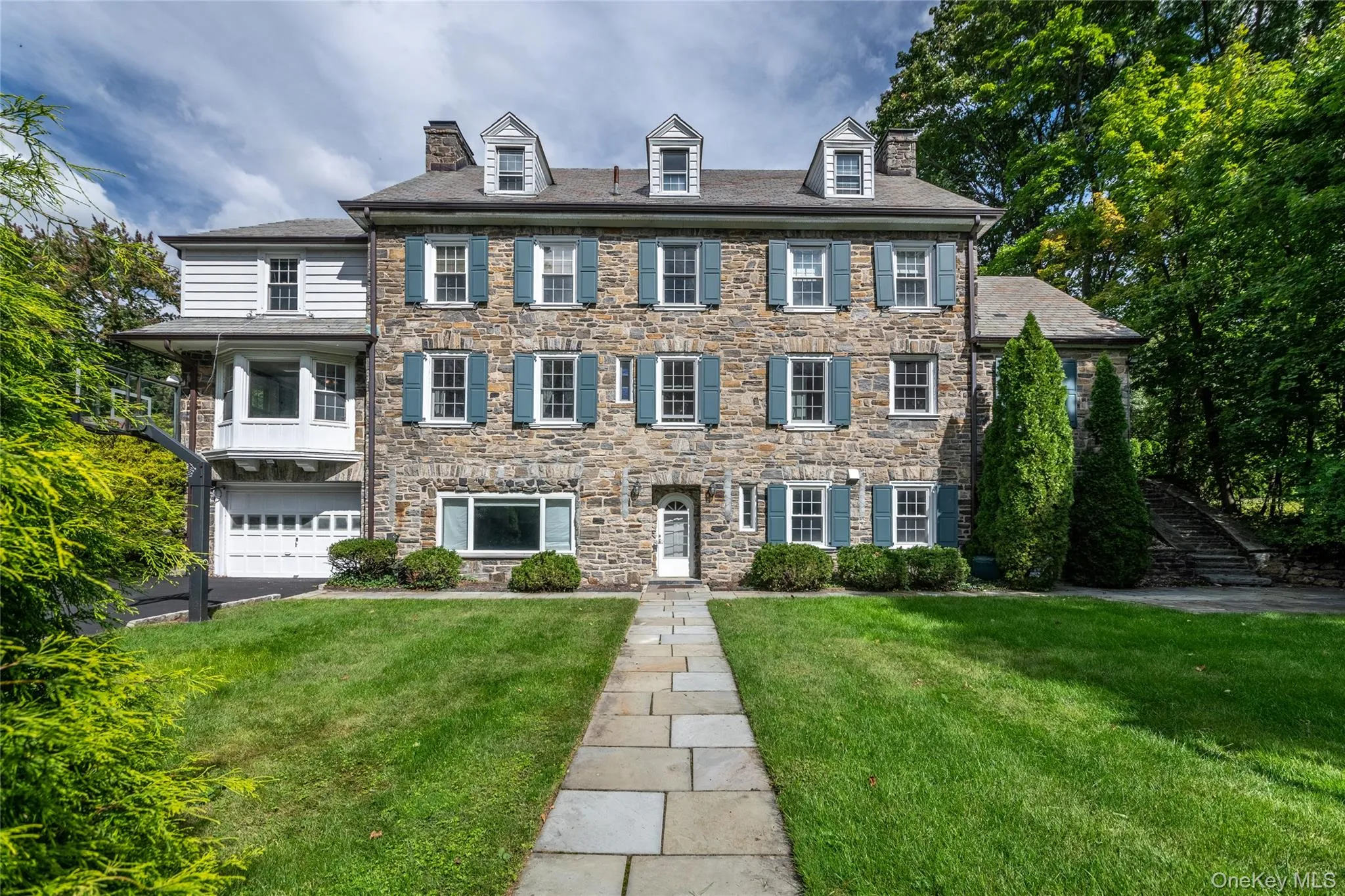Stone facade residence with multiple dormer windows, a prominent walkway, and an attached two-car garage Stone facade residence with multiple dormer windows, a prominent walkway, and an attached two-car garage