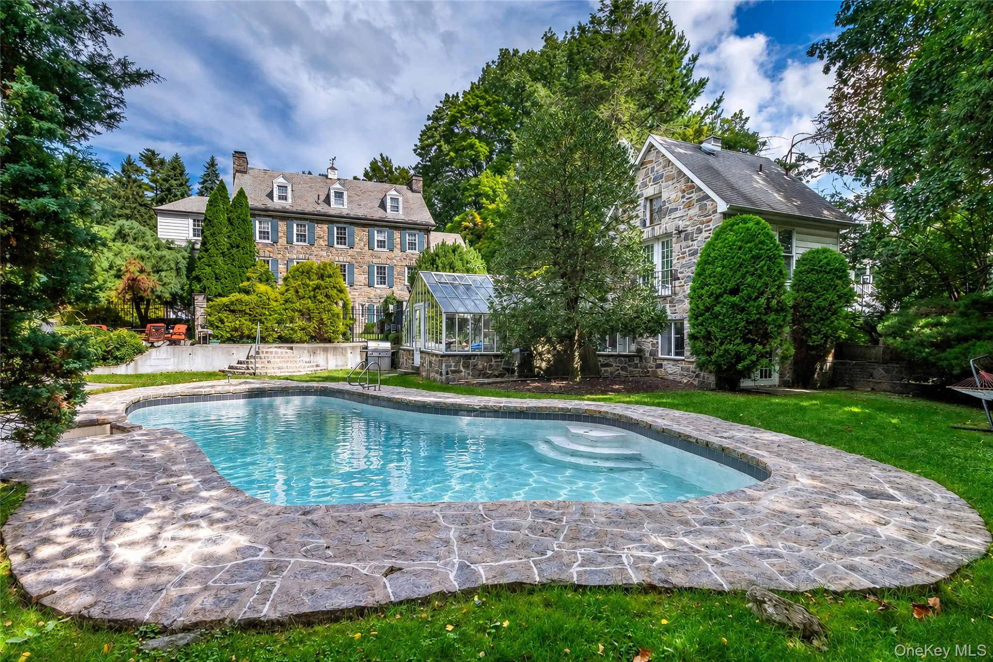 Curved swimming pool with integrated steps, surrounded by stone coping and a manicured lawn Curved swimming pool with integrated steps, surrounded by stone coping and a manicured lawn
