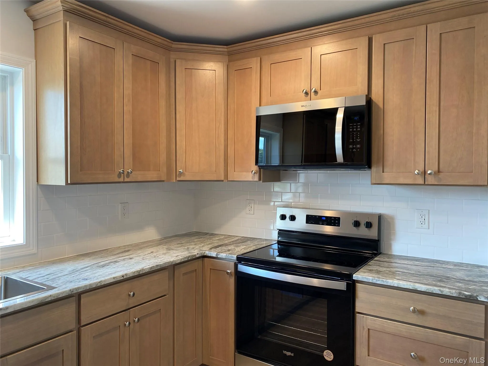 Kitchen featuring electric range oven, stainless steel microwave, tasteful backsplash, light stone counters, and brown cabinets Kitchen featuring electric range oven, stainless steel microwave, tasteful backsplash, light stone counters, and brown cabinets