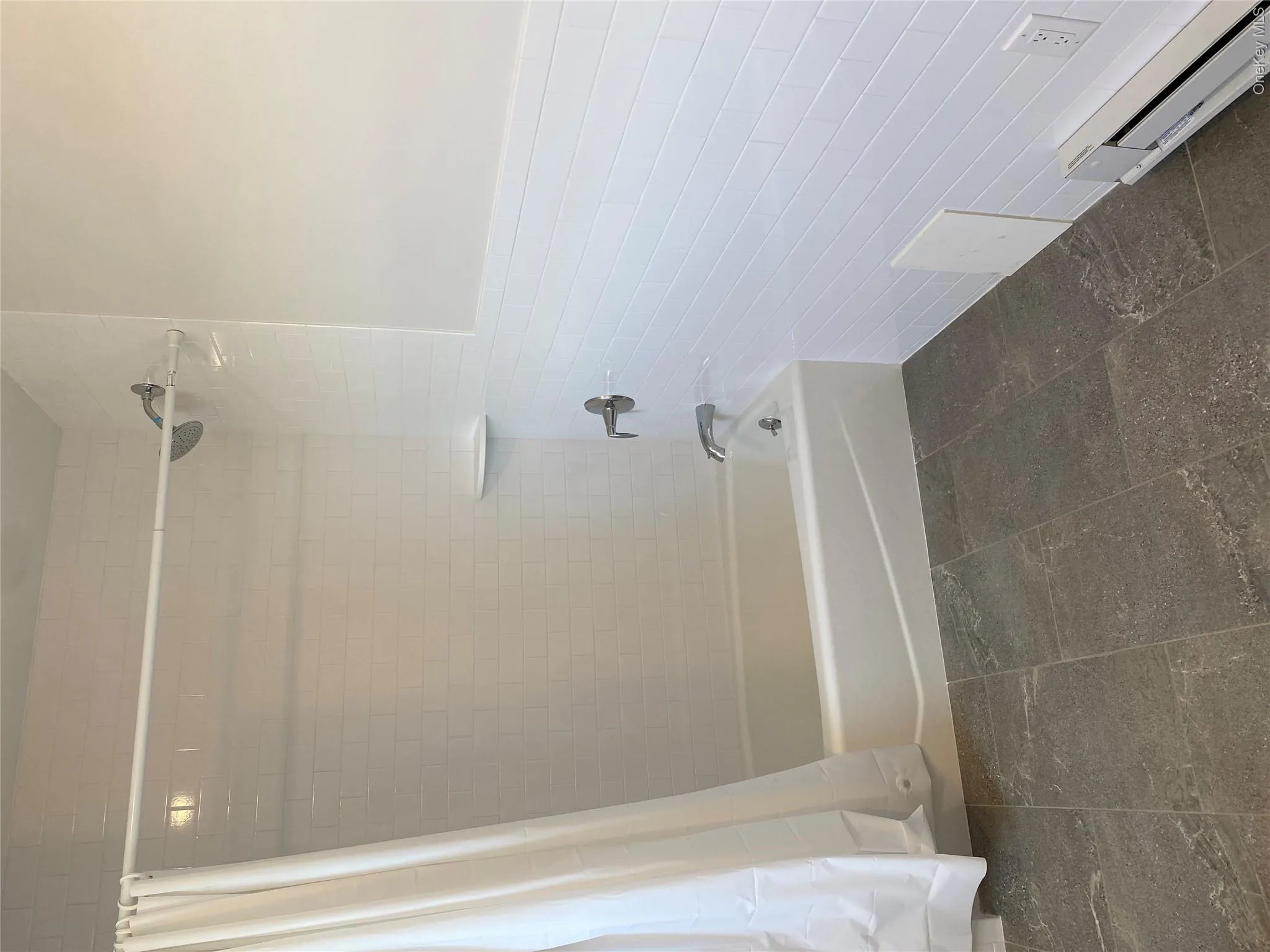 Bathroom featuring baseboard heating, shower / bathtub combination with curtain, tile walls, and a wainscoted wall Bathroom featuring baseboard heating, shower / bathtub combination with curtain, tile walls, and a wainscoted wall
