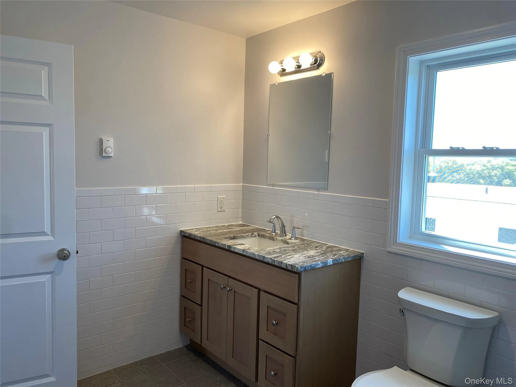 Half bathroom featuring tile walls, vanity, a wainscoted wall, and dark tile patterned flooring Half bathroom featuring tile walls, vanity, a wainscoted wall, and dark tile patterned flooring