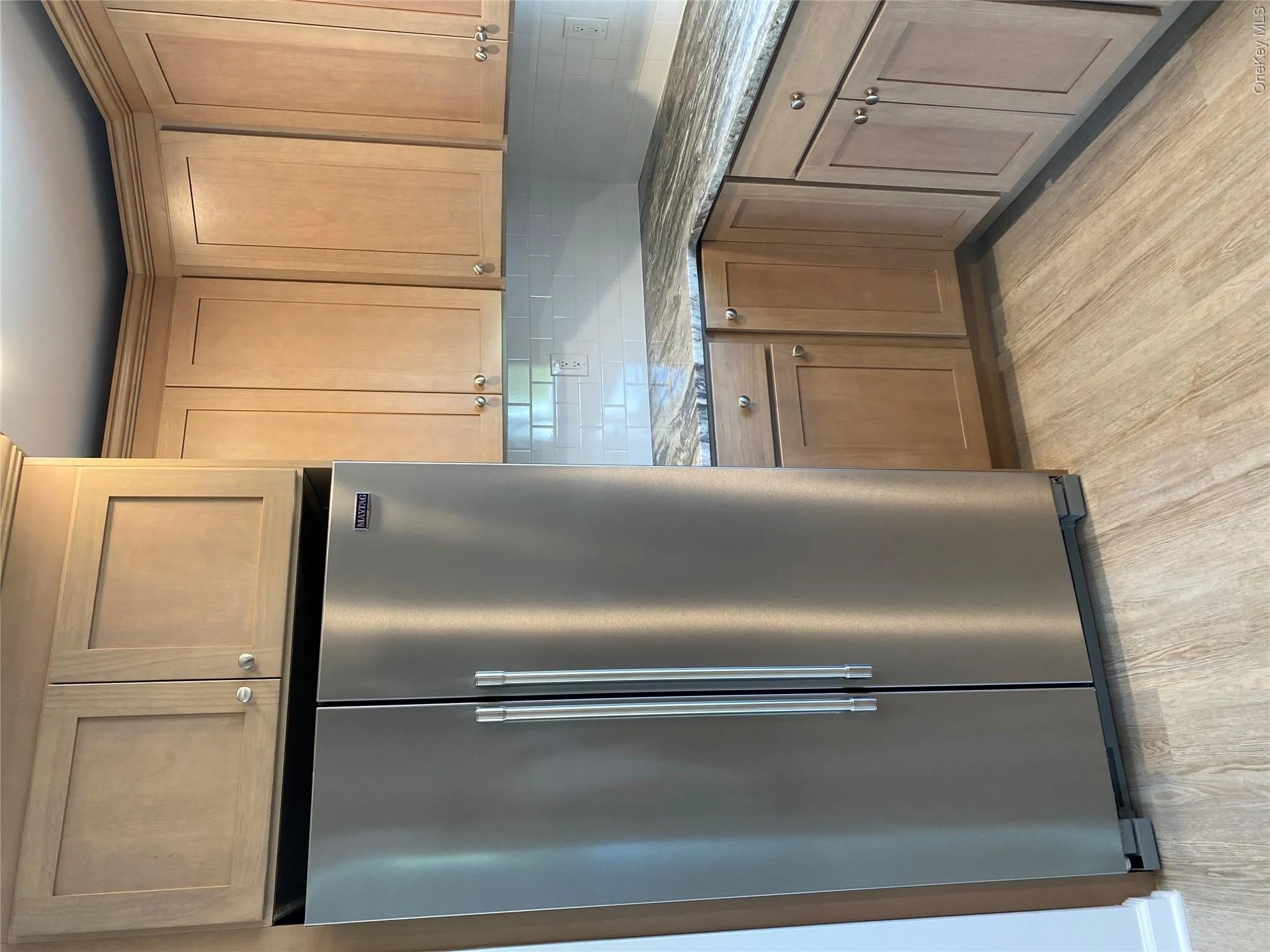 Kitchen with high end fridge, light stone counters, tasteful backsplash, light wood-style flooring, and brown cabinetry Kitchen with high end fridge, light stone counters, tasteful backsplash, light wood-style flooring, and brown cabinetry