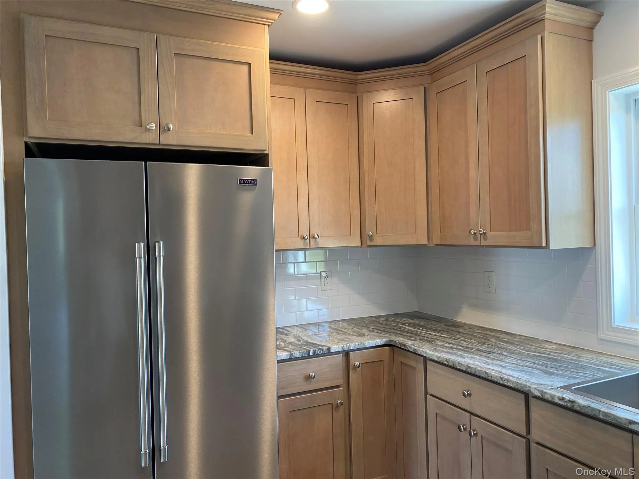 Kitchen featuring stainless steel built in refrigerator, backsplash, light stone counters, and brown cabinets Kitchen featuring stainless steel built in refrigerator, backsplash, light stone counters, and brown cabinets