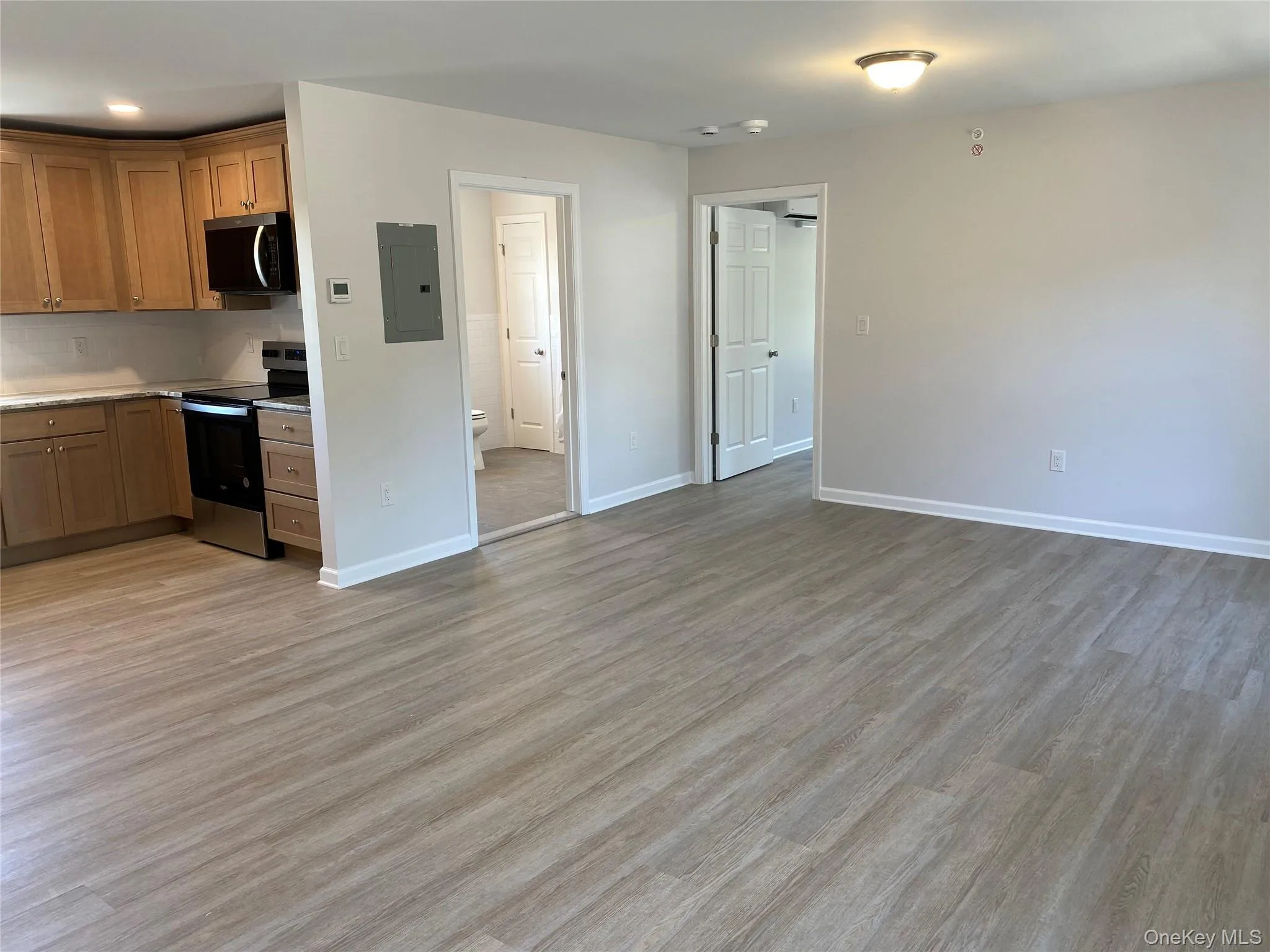 Kitchen featuring appliances with stainless steel finishes, light countertops, light wood-style flooring, electric panel, and brown cabinets Kitchen featuring appliances with stainless steel finishes, light countertops, light wood-style flooring, electric panel, and brown cabinets