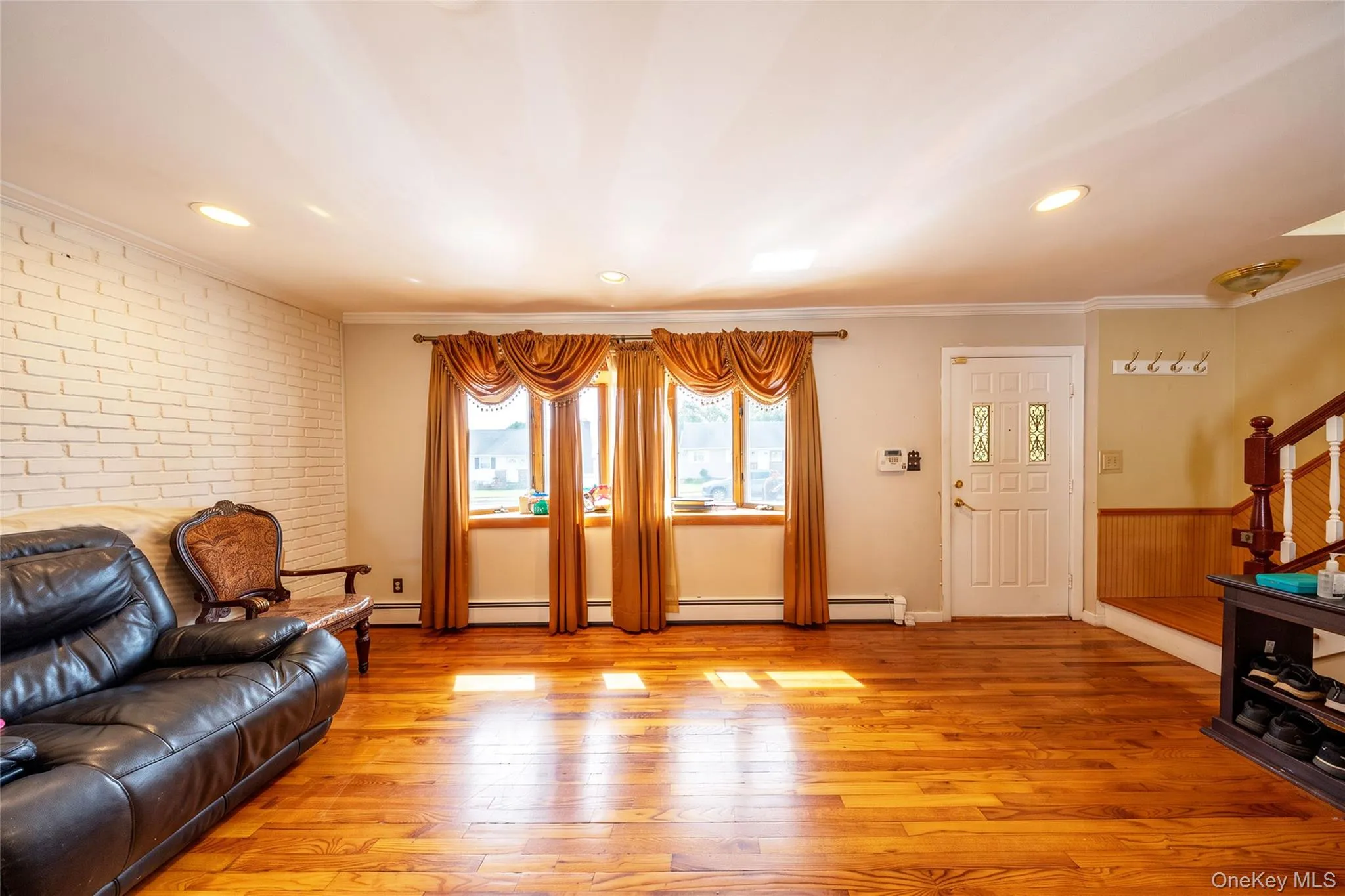 Hardwood flooring, recessed lighting, white brick accent wall, paneled entry door with decorative glass inserts, and wainscoting detail Hardwood flooring, recessed lighting, white brick accent wall, paneled entry door with decorative glass inserts, and wainscoting detail