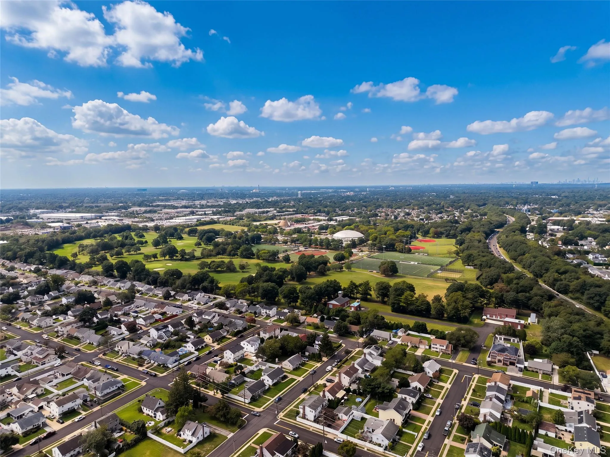 Aerial perspective of a residential community featuring a golf course, sports fields, and tree-lined streets Aerial perspective of a residential community featuring a golf course, sports fields, and tree-lined streets