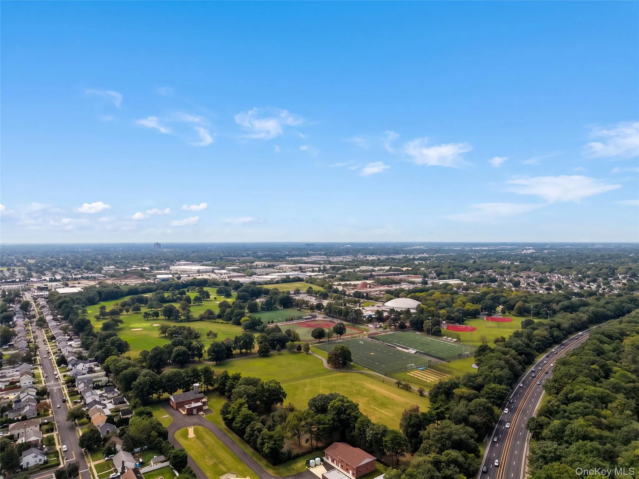 Expansive aerial perspective showcasing a golf course, sports fields, residential areas, and a multi-lane highway Expansive aerial perspective showcasing a golf course, sports fields, residential areas, and a multi-lane highway