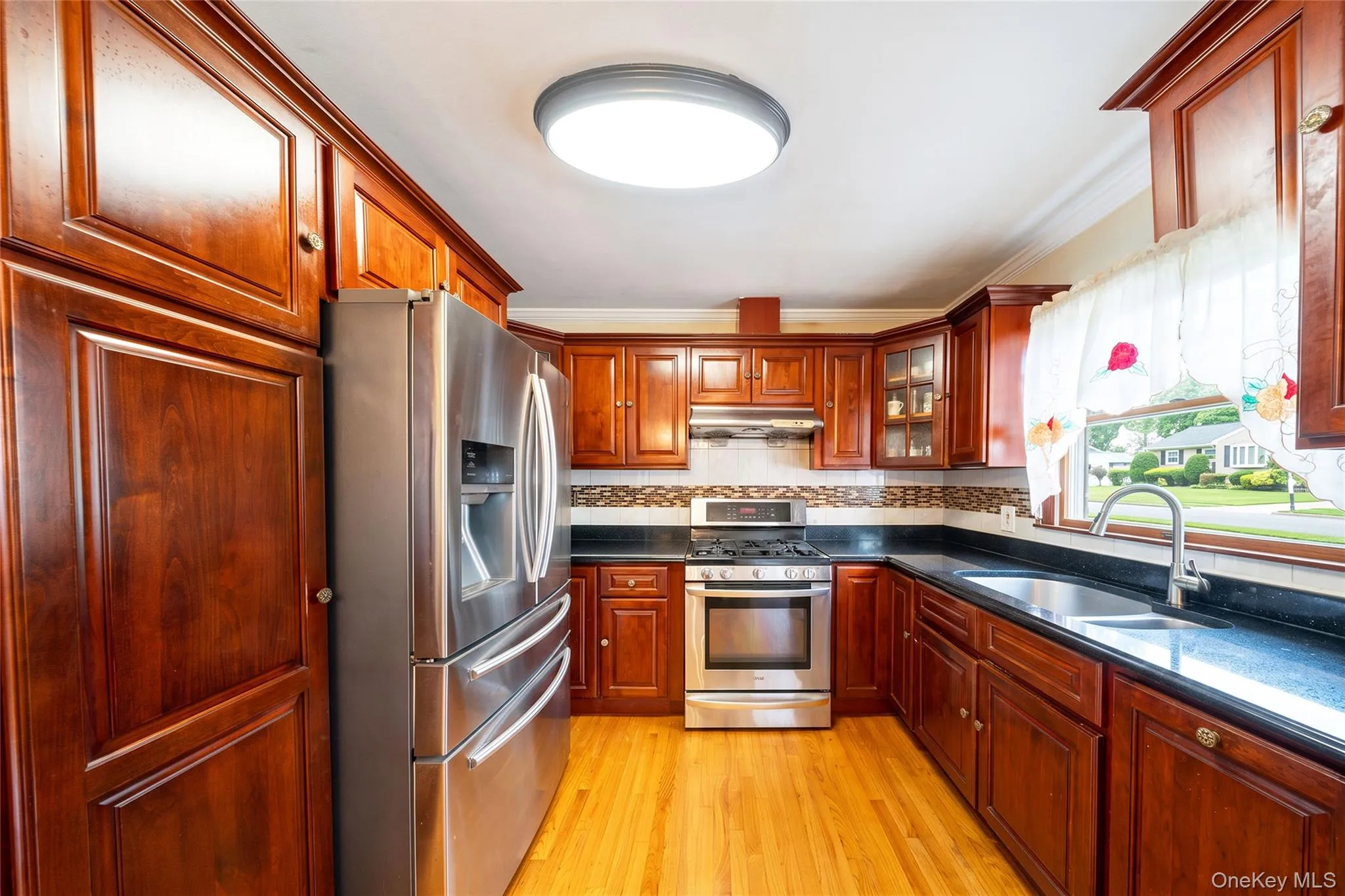 Kitchen featuring wood-finish flooring, dark stone-finish countertops, stainless steel appliances, and wood cabinetry Kitchen featuring wood-finish flooring, dark stone-finish countertops, stainless steel appliances, and wood cabinetry