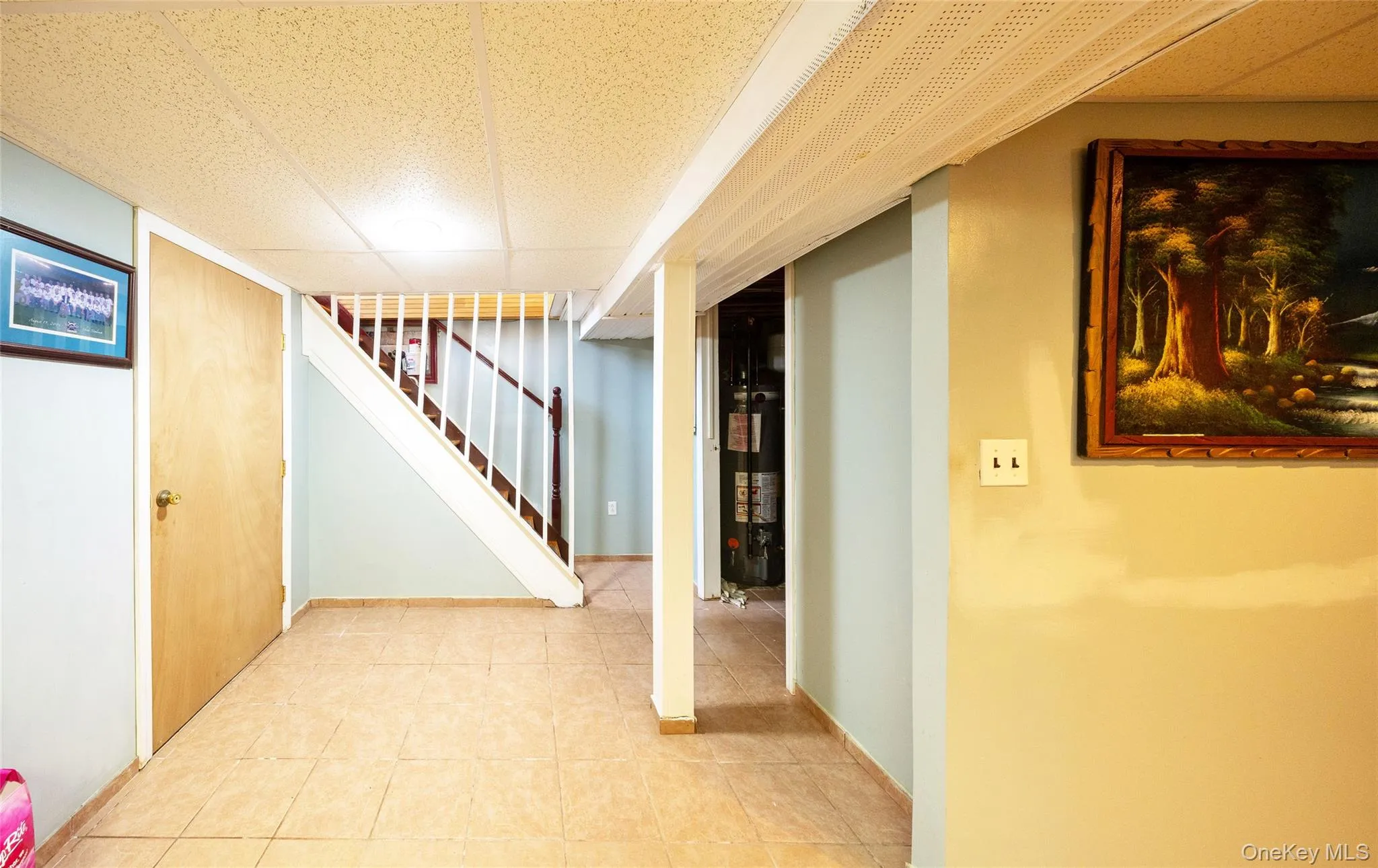 Tiled flooring, interior wood door, staircase with wood handrail and white balusters, painted walls, and ceiling with paneling Tiled flooring, interior wood door, staircase with wood handrail and white balusters, painted walls, and ceiling with paneling