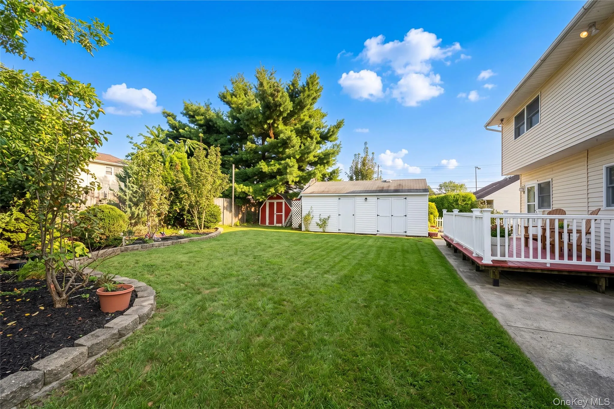 Expansive backyard featuring a manicured lawn, established landscaping, a multi-level wood deck with white railings, and two storage sheds Expansive backyard featuring a manicured lawn, established landscaping, a multi-level wood deck with white railings, and two storage sheds