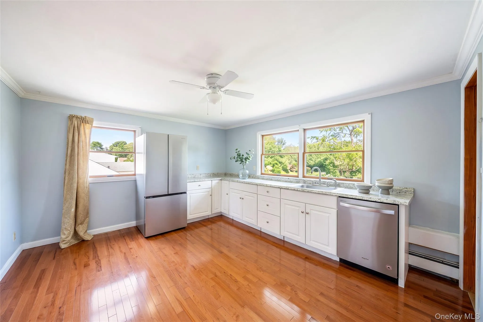 Wood-finish flooring throughout, white cabinetry with silver-tone hardware, stainless steel appliances, and a ceiling fan with light Wood-finish flooring throughout, white cabinetry with silver-tone hardware, stainless steel appliances, and a ceiling fan with light