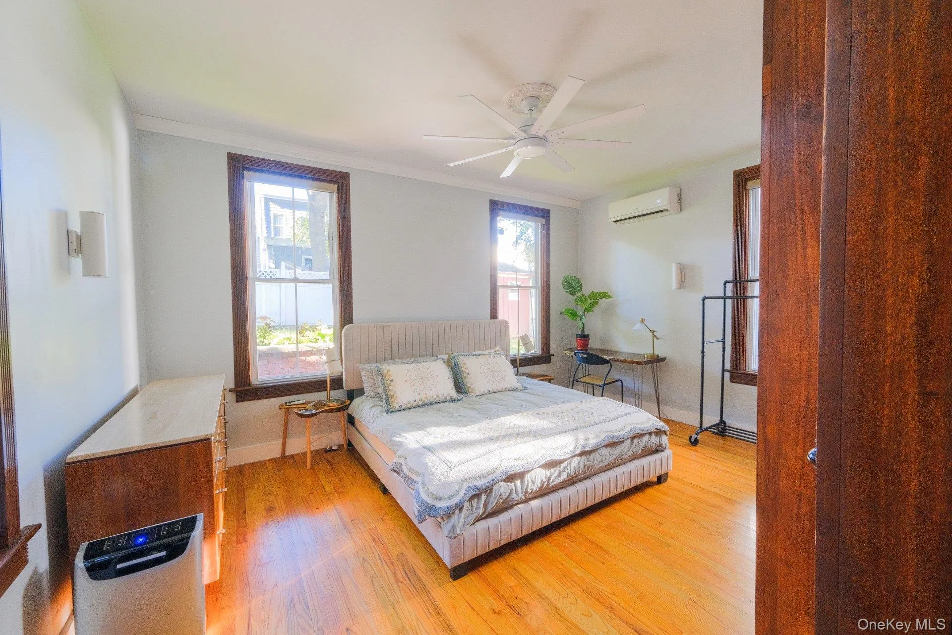 Hardwood flooring, multiple windows with wood trim, ceiling fan, and wall-mounted air conditioning unit Hardwood flooring, multiple windows with wood trim, ceiling fan, and wall-mounted air conditioning unit