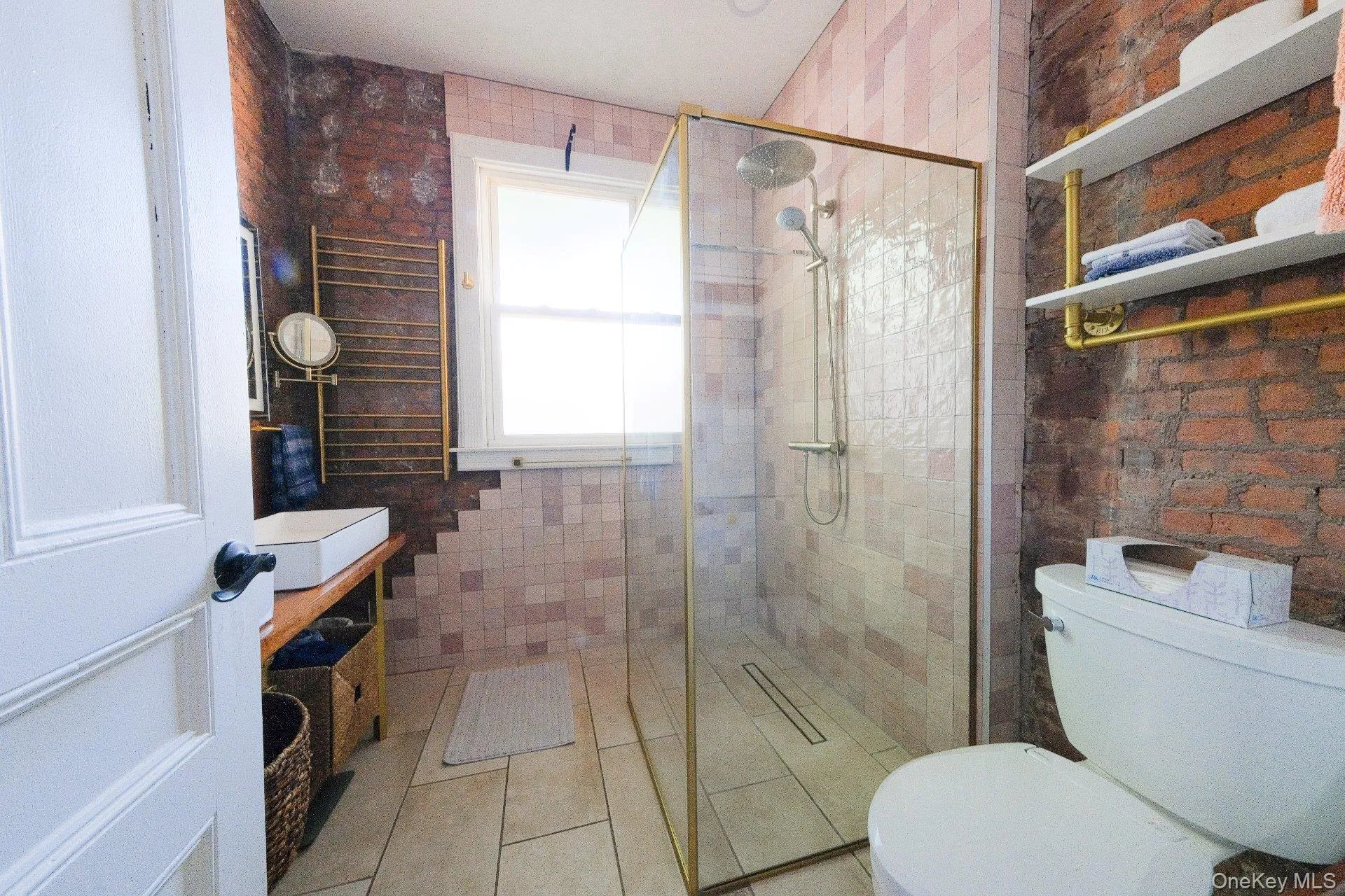 Glass-enclosed shower with gold-tone fixtures, floor-level linear drain, and tiled walls Glass-enclosed shower with gold-tone fixtures, floor-level linear drain, and tiled walls