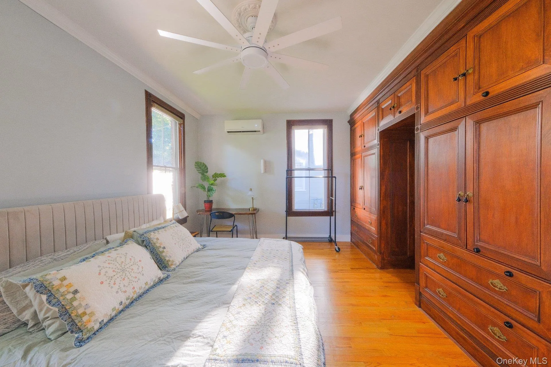 Hardwood flooring, wood-finish built-in cabinetry, crown molding, white ceiling fan, and wall-mounted air conditioning unit Hardwood flooring, wood-finish built-in cabinetry, crown molding, white ceiling fan, and wall-mounted air conditioning unit