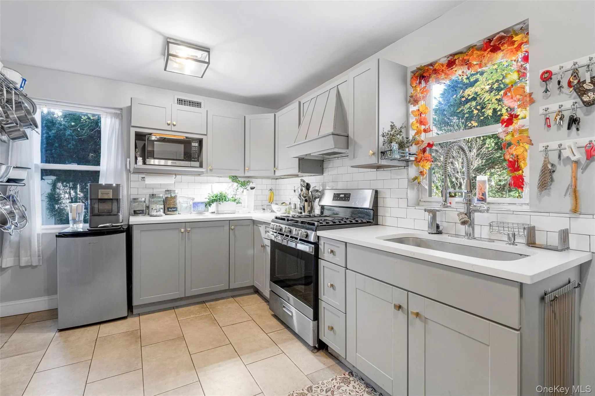 Kitchen featuring a wealth of natural light, custom range hood, gray cabinetry, and appliances with stainless steel finishes Kitchen featuring a wealth of natural light, custom range hood, gray cabinetry, and appliances with stainless steel finishes