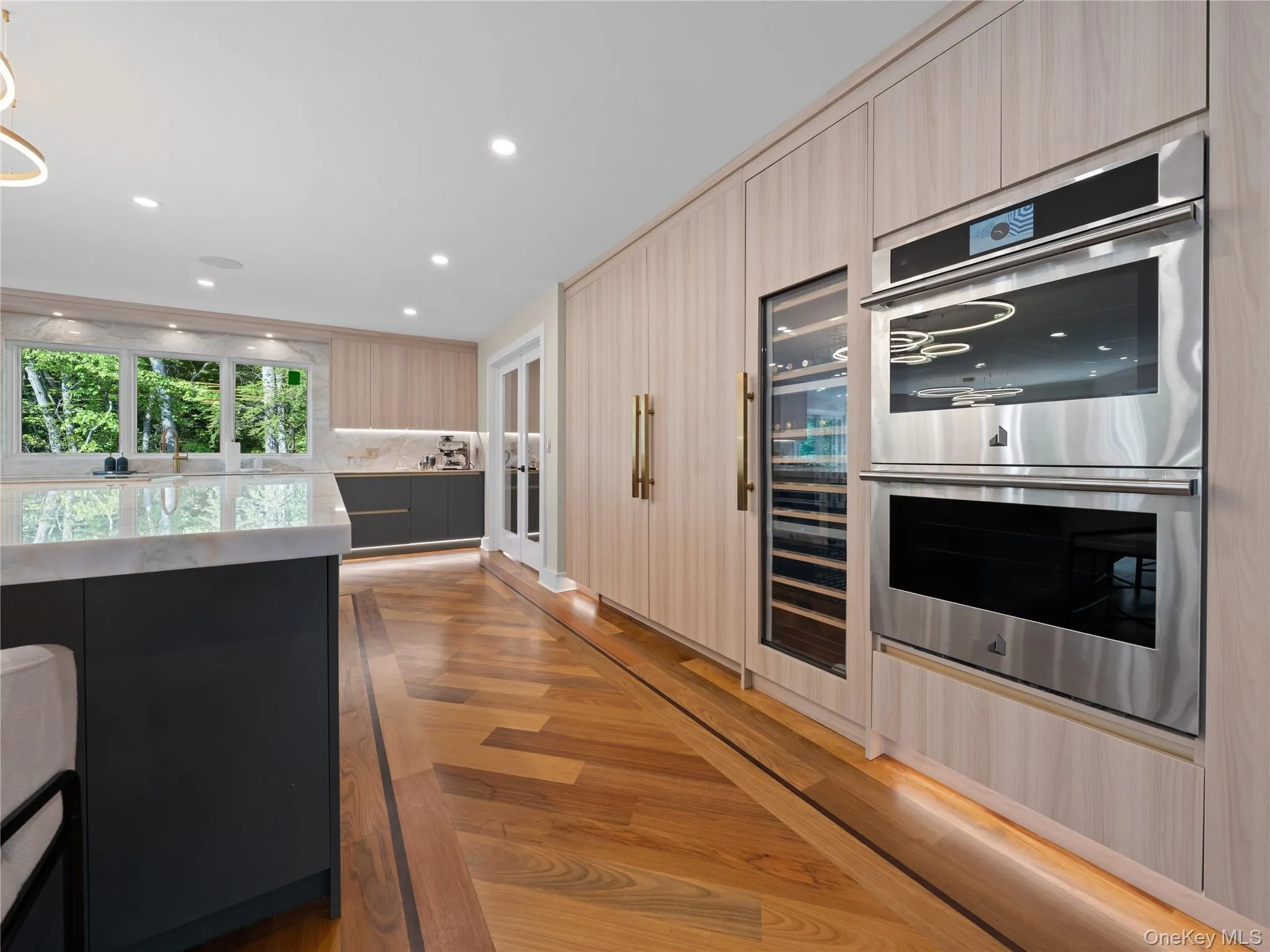 Kitchen with double oven, light stone countertops, dark cabinetry, wine cooler, and modern cabinets Kitchen with double oven, light stone countertops, dark cabinetry, wine cooler, and modern cabinets