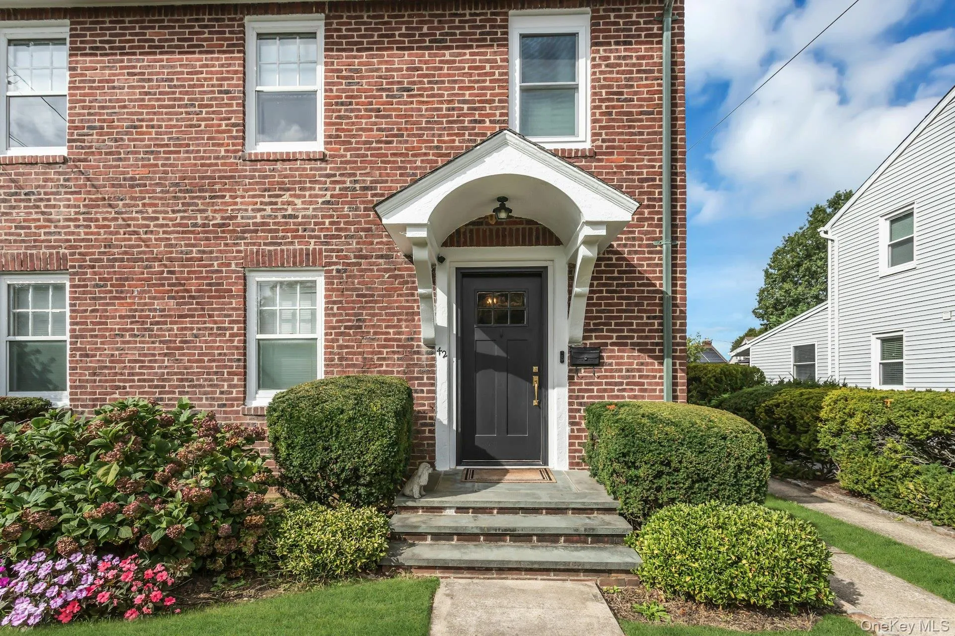 Red brick exterior with white trim windows and a dark panel front door, brick walkway and bluestone steps Red brick exterior with white trim windows and a dark panel front door, brick walkway and bluestone steps